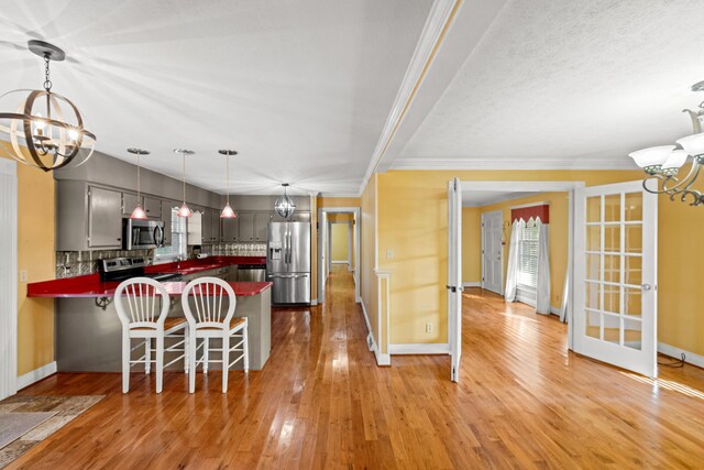 kitchen with a notable chandelier, kitchen peninsula, hardwood / wood-style floors, decorative backsplash, and appliances with stainless steel finishes