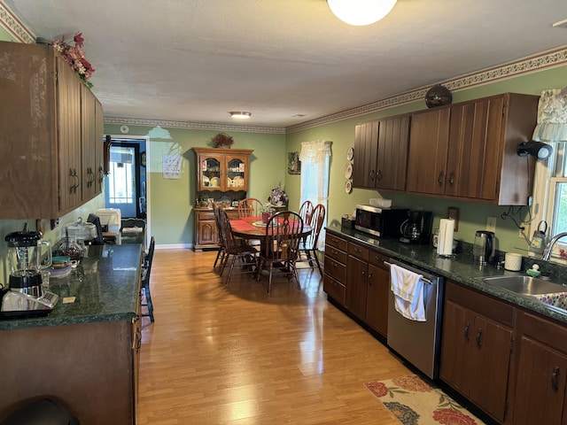 kitchen with stainless steel dishwasher, dark countertops, light wood-type flooring, and a sink