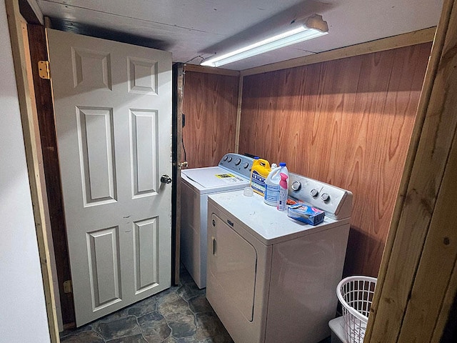 clothes washing area featuring separate washer and dryer, dark tile patterned flooring, and wood walls