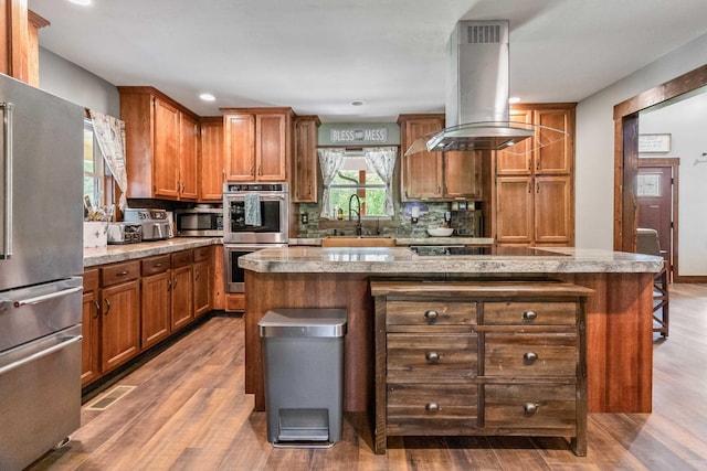 kitchen featuring appliances with stainless steel finishes, sink, wood-type flooring, a kitchen island, and island range hood