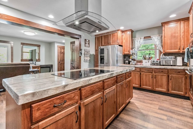 kitchen with a center island, black electric cooktop, high quality fridge, wall chimney range hood, and light wood-type flooring