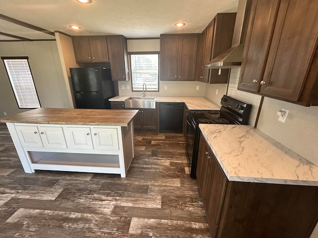 kitchen with dark brown cabinets, black appliances, a center island, sink, and wall chimney range hood