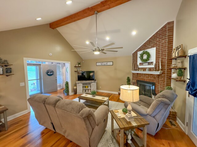 living room with beamed ceiling, high vaulted ceiling, a brick fireplace, wood-type flooring, and ceiling fan