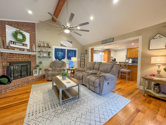 living room featuring a brick fireplace, light hardwood / wood-style floors, beamed ceiling, ceiling fan, and high vaulted ceiling