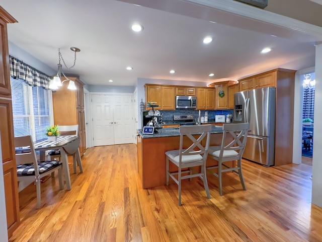 kitchen with light wood-type flooring, dark stone countertops, an inviting chandelier, appliances with stainless steel finishes, and a breakfast bar area