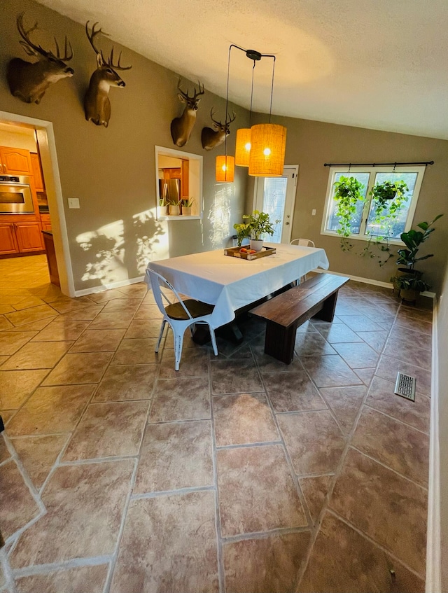 dining space with vaulted ceiling, a textured ceiling, and tile patterned floors