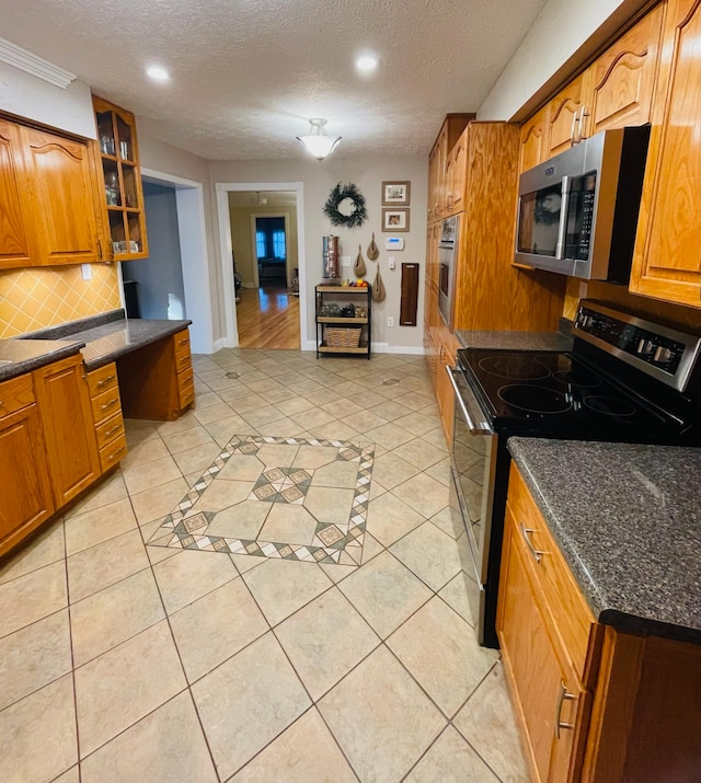 kitchen with light tile patterned floors, a textured ceiling, stainless steel appliances, and decorative backsplash