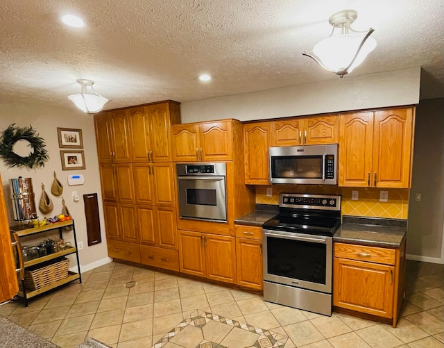 kitchen with a textured ceiling, light tile patterned floors, appliances with stainless steel finishes, and decorative backsplash