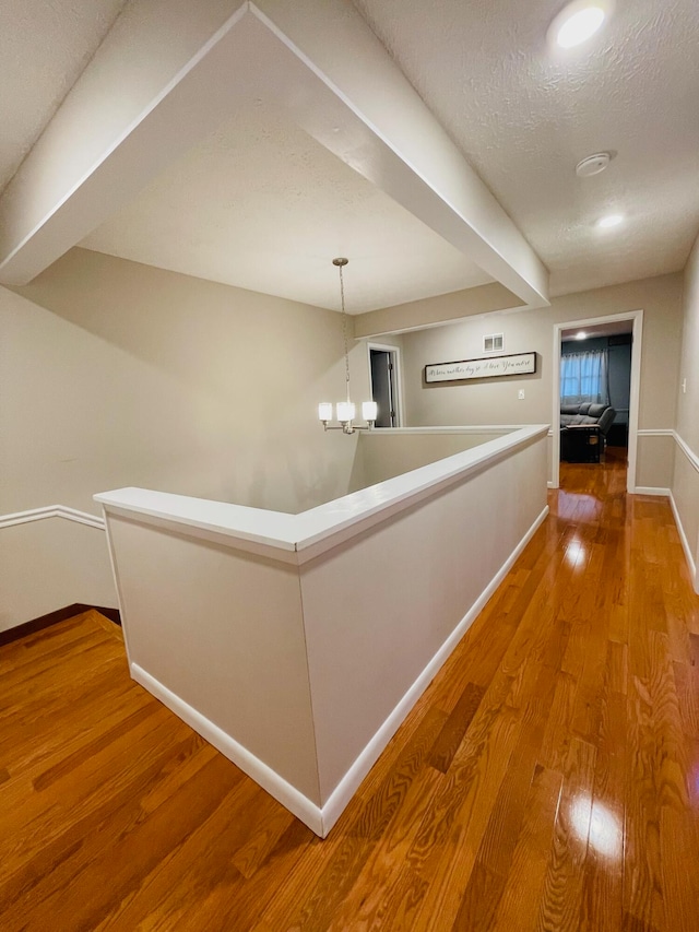 hall featuring a textured ceiling, a notable chandelier, and hardwood / wood-style floors