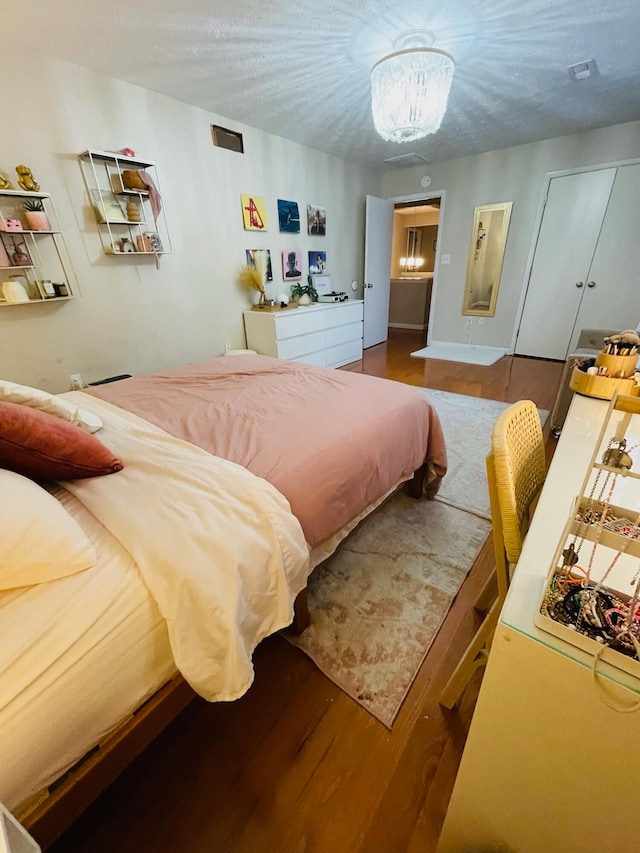 bedroom with a textured ceiling, hardwood / wood-style flooring, and an inviting chandelier