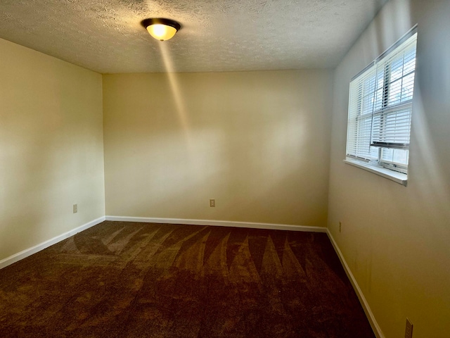 spare room featuring a textured ceiling and dark carpet