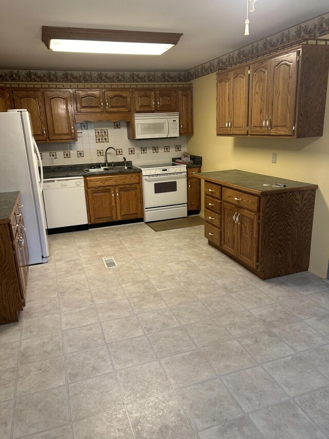 kitchen with white appliances, a sink, dark countertops, tasteful backsplash, and brown cabinetry