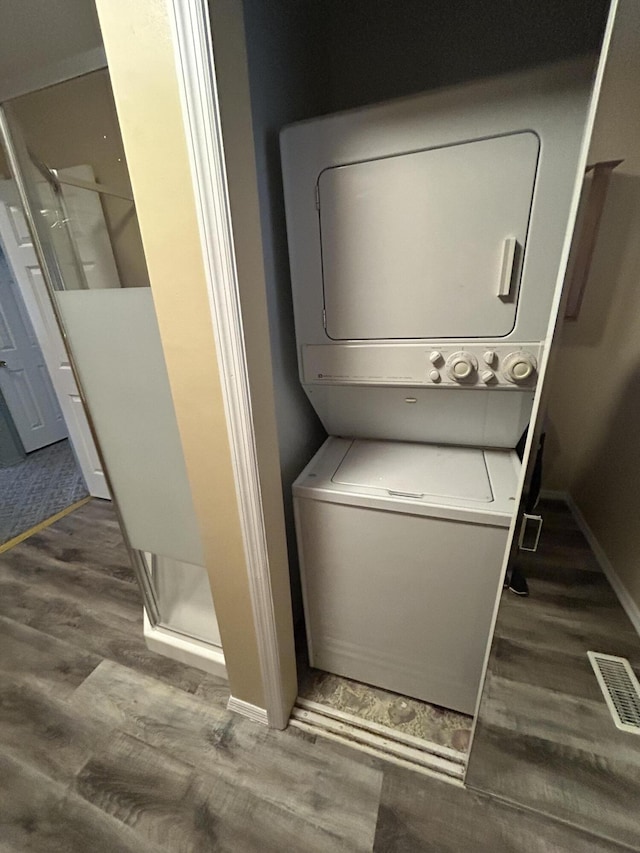 clothes washing area featuring estacked washer and dryer, wood finished floors, and baseboards