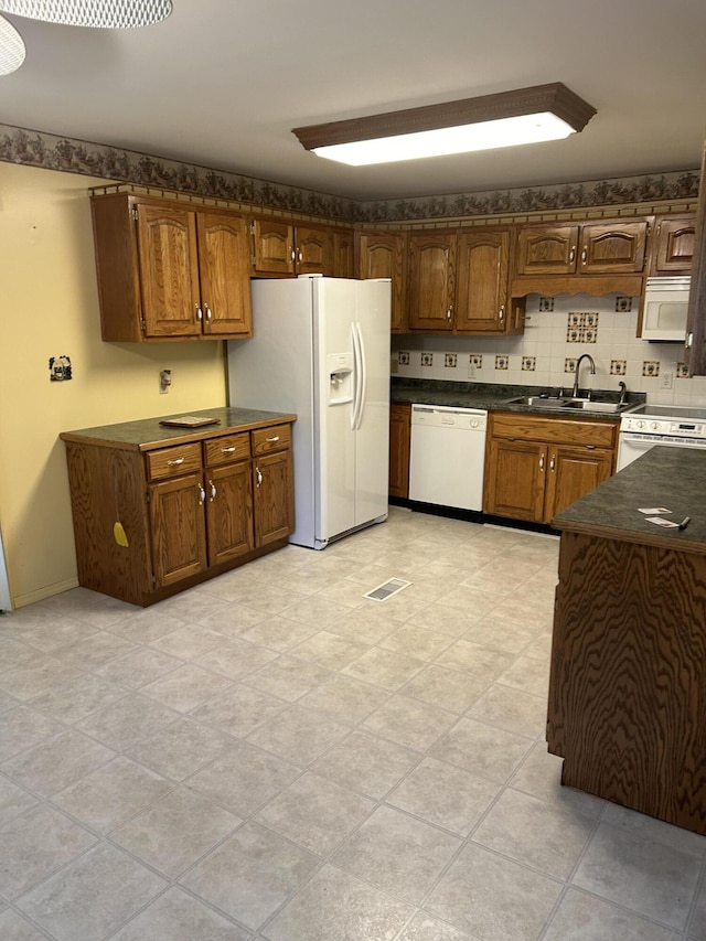 kitchen featuring white appliances, a sink, dark countertops, brown cabinetry, and decorative backsplash