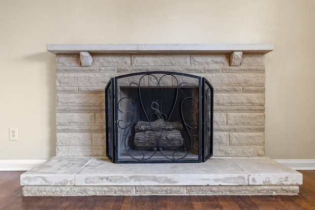 details featuring a fireplace with raised hearth, wood finished floors, and baseboards