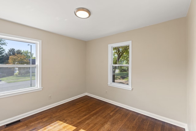 spare room with dark wood-type flooring, visible vents, and baseboards