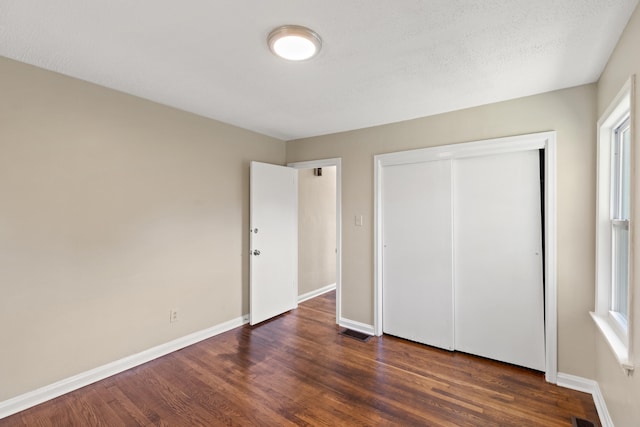 unfurnished bedroom featuring a closet, wood finished floors, visible vents, and baseboards