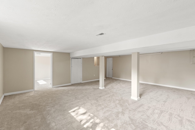 finished below grade area featuring electric panel, visible vents, baseboards, light colored carpet, and a textured ceiling