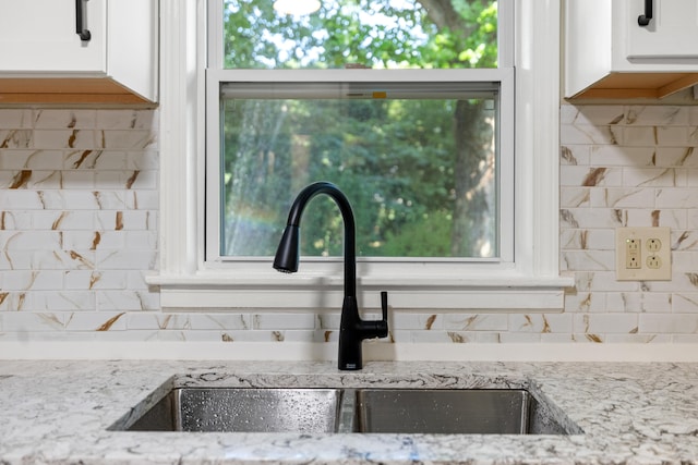 kitchen featuring backsplash, a sink, white cabinetry, and light stone countertops