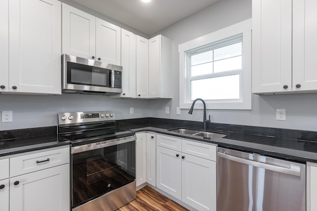 kitchen featuring dark stone countertops, sink, white cabinets, appliances with stainless steel finishes, and hardwood / wood-style flooring