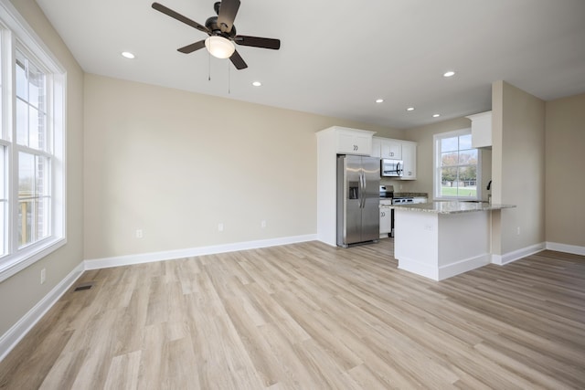 kitchen featuring kitchen peninsula, appliances with stainless steel finishes, light wood-type flooring, light stone counters, and white cabinets