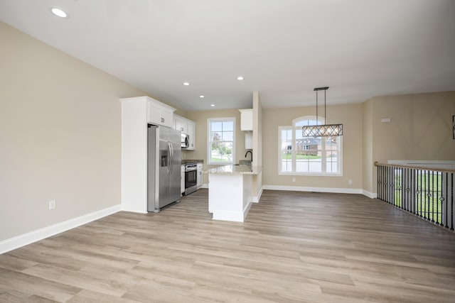 kitchen featuring white cabinets, stainless steel appliances, hanging light fixtures, and light hardwood / wood-style flooring