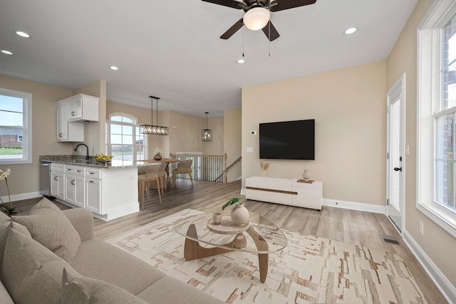 living room with ceiling fan with notable chandelier, light hardwood / wood-style floors, plenty of natural light, and sink