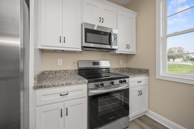 kitchen featuring white cabinets, light stone counters, stainless steel appliances, and hardwood / wood-style floors