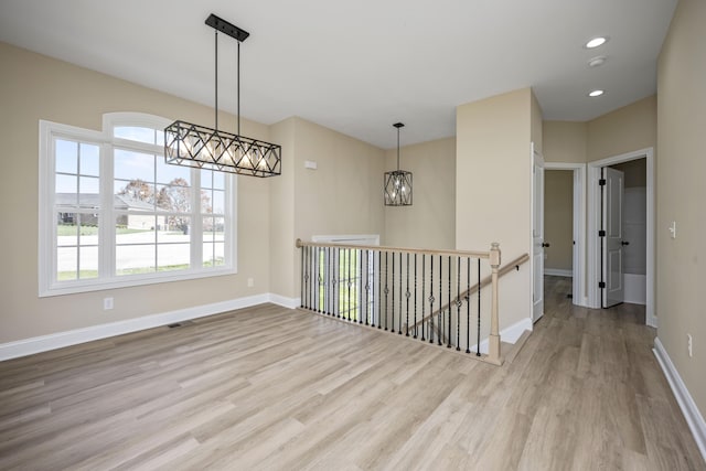 spare room with an inviting chandelier and light hardwood / wood-style flooring