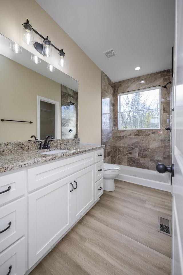 bathroom featuring hardwood / wood-style flooring, vanity, toilet, and tiled shower