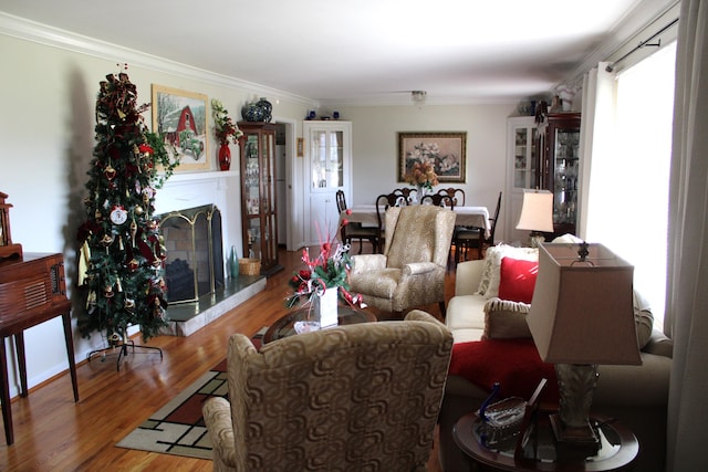 living room with a fireplace with raised hearth, ornamental molding, and wood finished floors