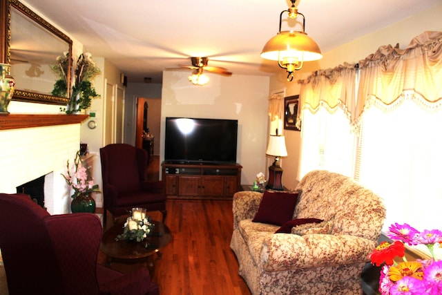 living room with a brick fireplace, ceiling fan, and wood finished floors