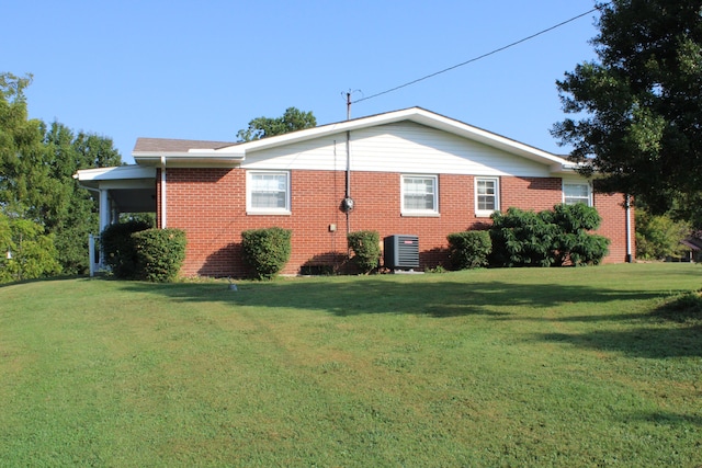 view of side of property featuring brick siding, central AC unit, and a yard