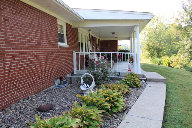 view of side of home featuring covered porch, a lawn, and brick siding