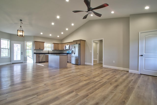 kitchen featuring decorative light fixtures, high vaulted ceiling, light hardwood / wood-style flooring, appliances with stainless steel finishes, and a kitchen island