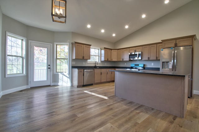 kitchen with appliances with stainless steel finishes, hardwood / wood-style flooring, high vaulted ceiling, a kitchen island, and sink