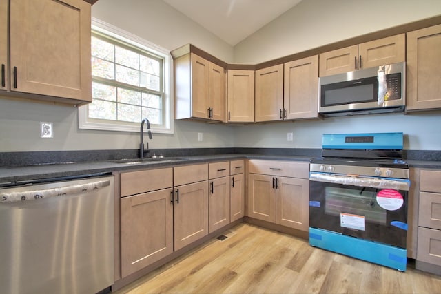 kitchen with dark stone countertops, appliances with stainless steel finishes, sink, light hardwood / wood-style flooring, and lofted ceiling