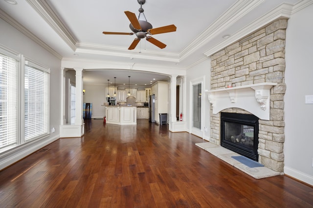 unfurnished living room featuring dark wood-style flooring, a fireplace, a ceiling fan, a tray ceiling, and decorative columns