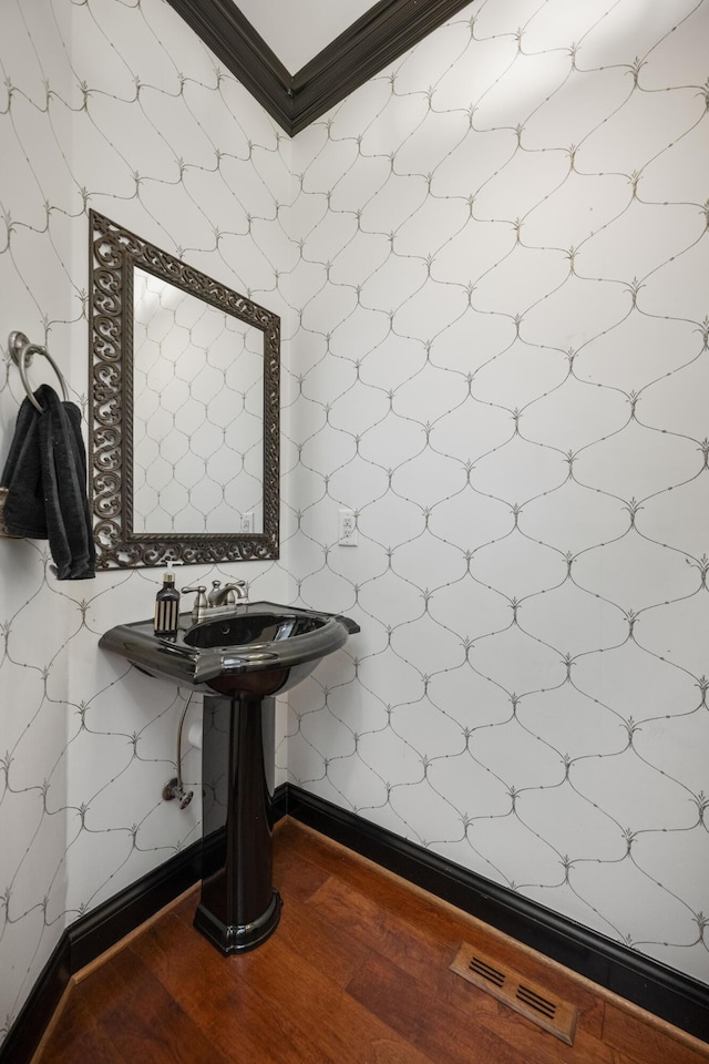 bathroom featuring baseboards, visible vents, crown molding, and wood finished floors