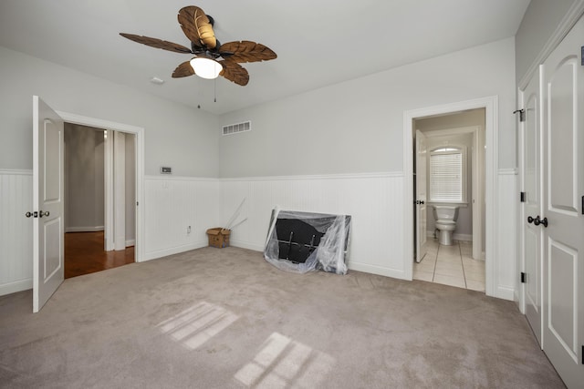 interior space with carpet flooring, visible vents, a ceiling fan, wainscoting, and ensuite bath