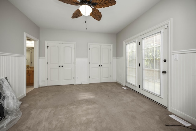 unfurnished bedroom with carpet, multiple closets, wainscoting, and access to exterior