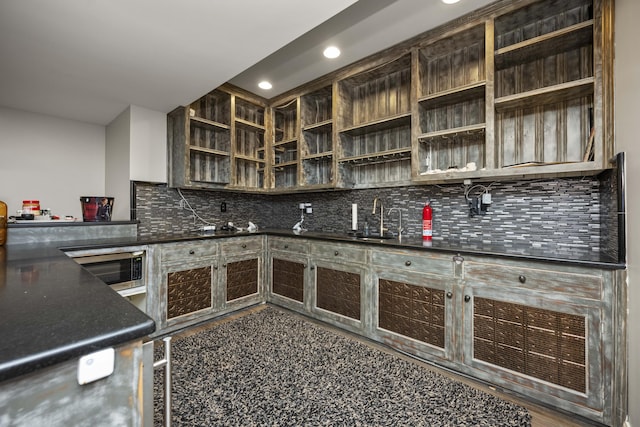 kitchen with decorative backsplash, dark countertops, stainless steel microwave, open shelves, and a sink