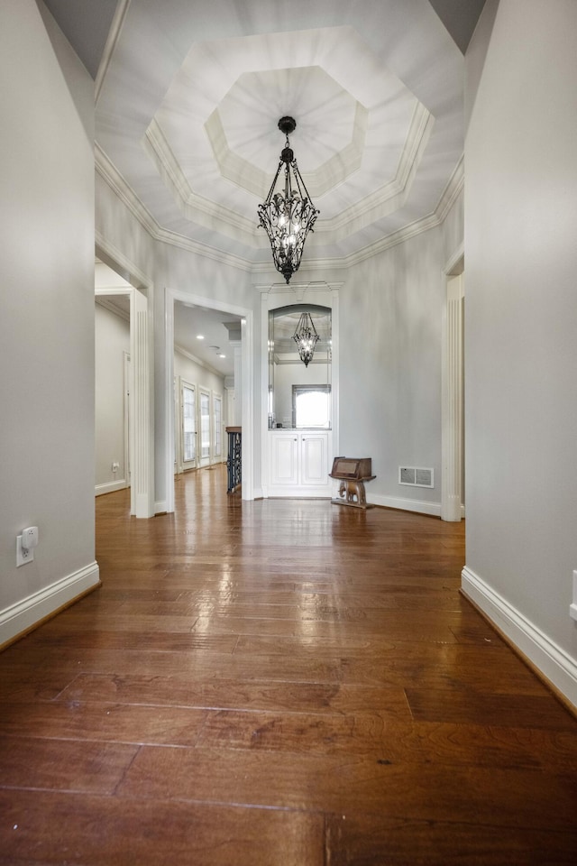 interior space with baseboards, visible vents, hardwood / wood-style floors, a tray ceiling, and a chandelier