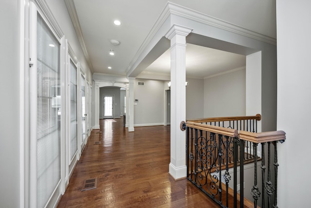 hallway with visible vents, baseboards, hardwood / wood-style floors, decorative columns, and crown molding