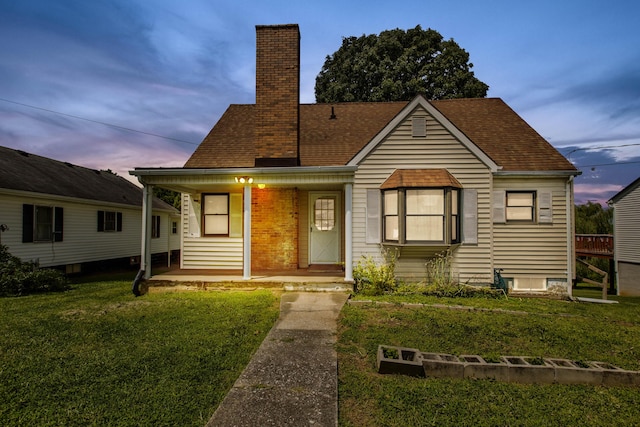 view of front of home with a shingled roof, a chimney, a porch, and a front yard