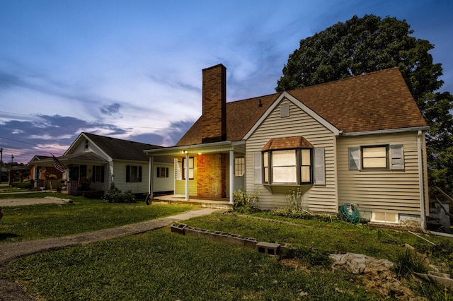 view of front of home featuring a porch, a front yard, a shingled roof, and a chimney