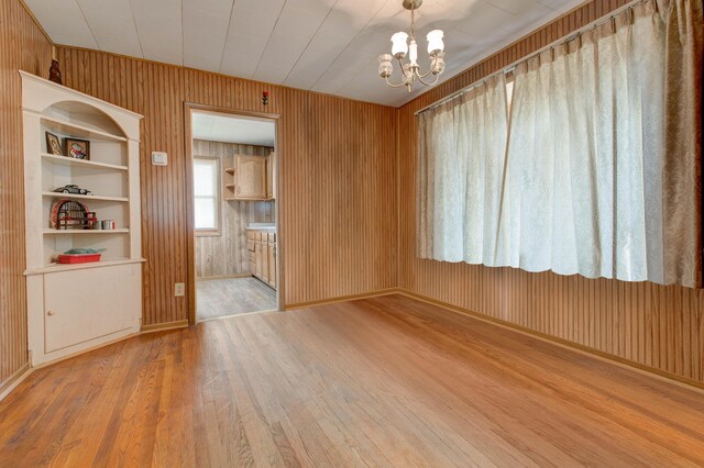 unfurnished room featuring a notable chandelier, light wood-type flooring, and wooden walls