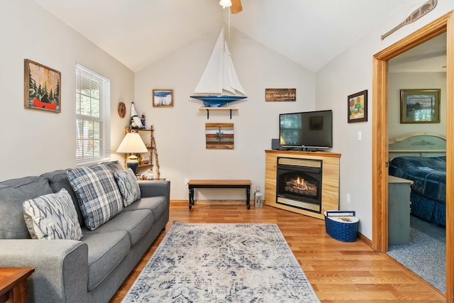 living area with baseboards, a warm lit fireplace, wood finished floors, and vaulted ceiling