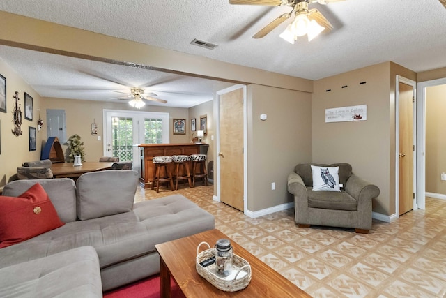 living area featuring visible vents, baseboards, light floors, a textured ceiling, and a bar