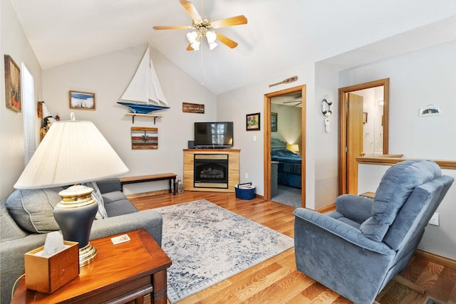 living area featuring baseboards, ceiling fan, vaulted ceiling, a fireplace, and wood finished floors